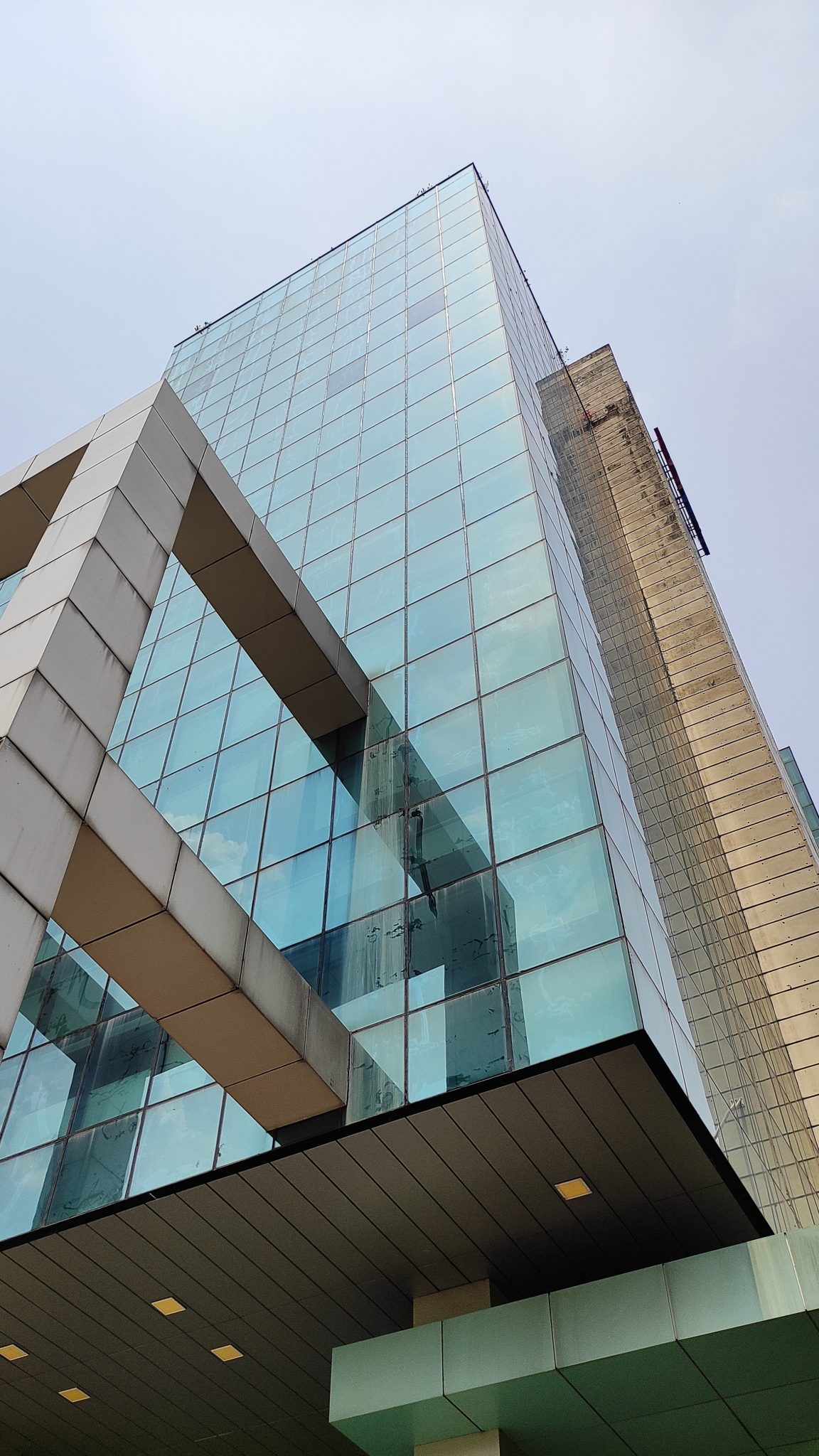 A modern glass building with a unique architectural design, showcasing large glass panels and geometric shapes. The image is taken from a low angle, emphasizing the height and structure of the buildin...