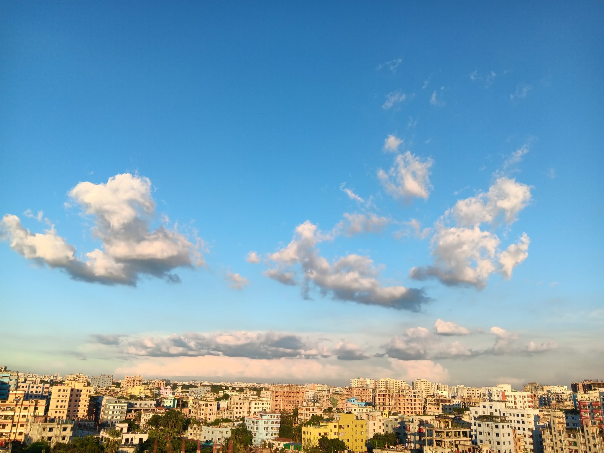 A panoramic view of a city skyline against a bright blue sky, dotted with fluffy white clouds.