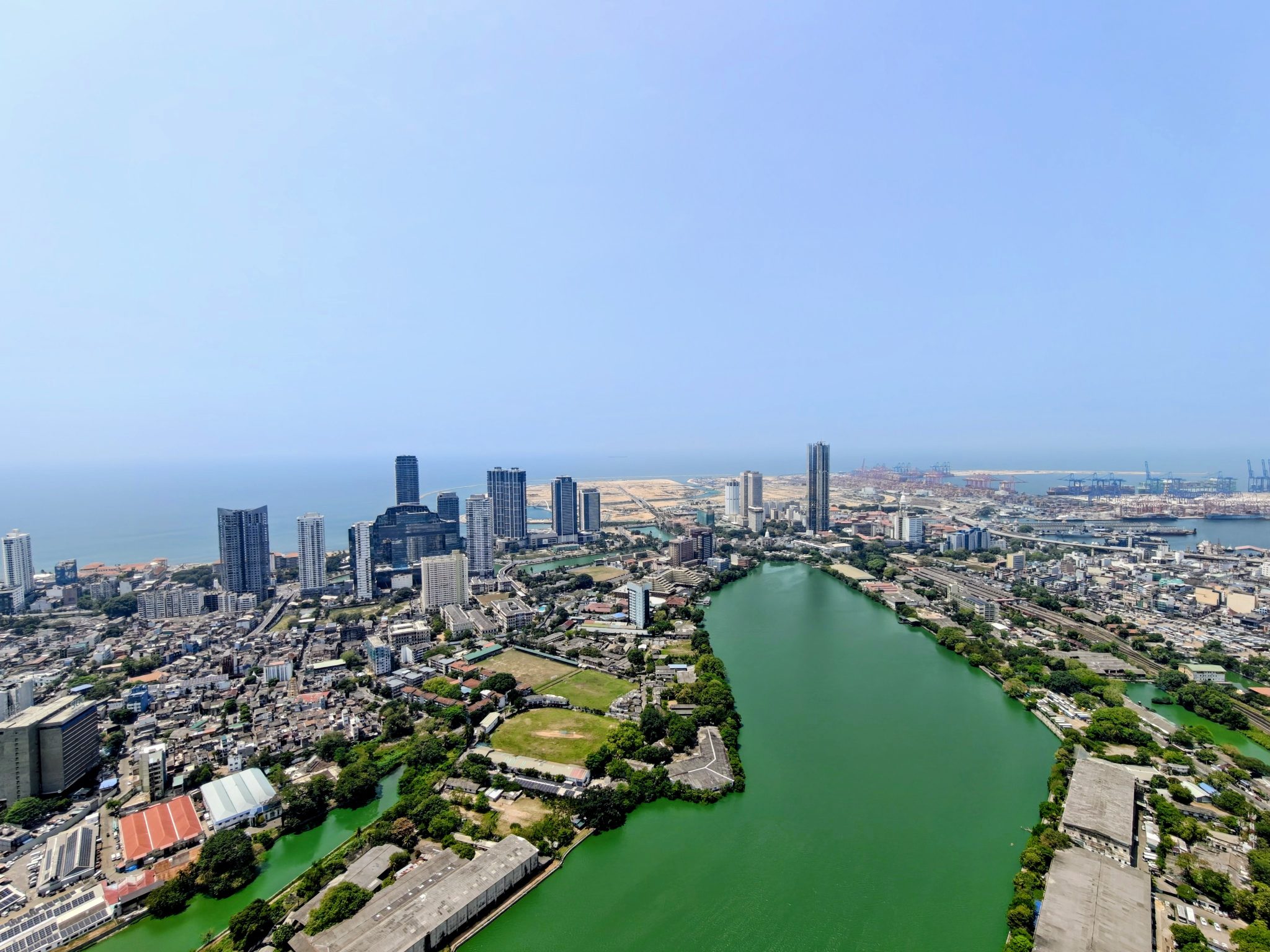 Aerial view of Colombo, Sri Lanka, captured from the top of the Lotus Tower, showing the city skyline, Beira Lake, surrounding urban areas, and the Indian Ocean coastline in the distance.