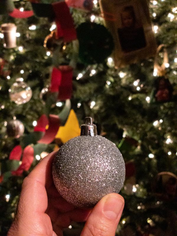 Christmas ornament held in front of a lit Christmas tree