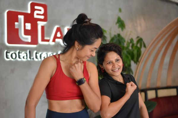 Middle Aged Asian Woman Flexing her Biceps at the Gym with her Personal Trainer