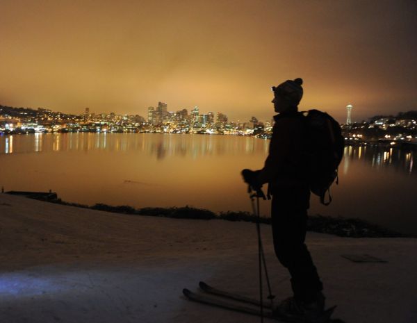 On record snow, night skier with pack and head light, city reflected in Lake Union, Space Needle, from the top of the hill, Gas Works Park, Wallingford, Seattle, Washington, USA