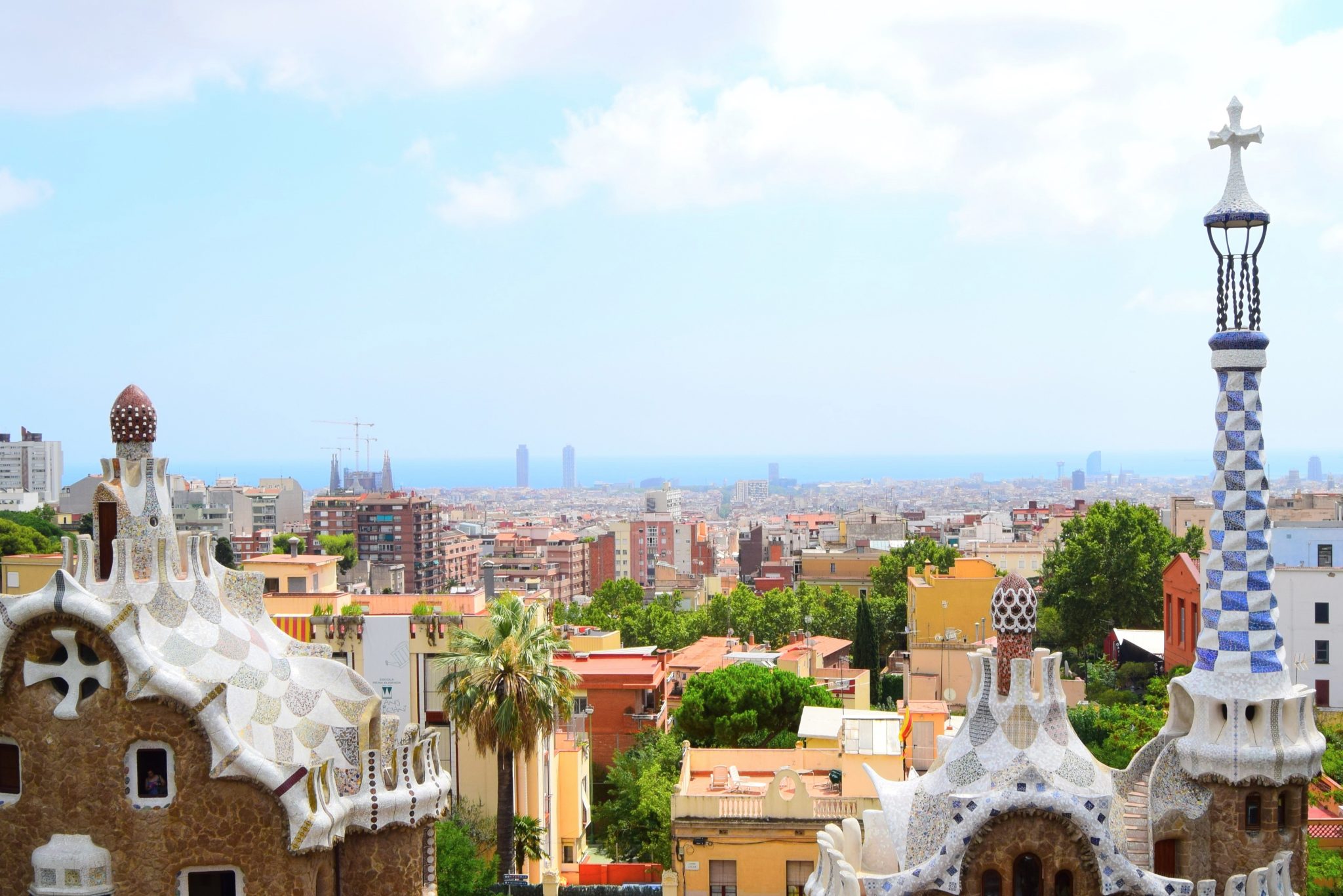 Panoramic view of Barcelona from Park Güell, featuring Gaudi’s mosaic-tiled rooftops and spires in the foreground against the city skyline and Mediterranean Sea.