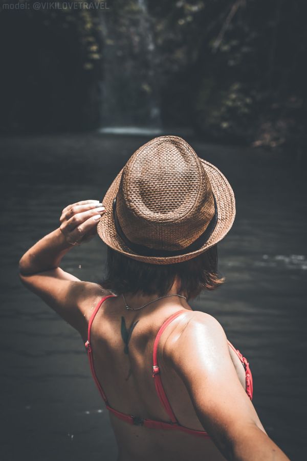 Rear view of young woman tourist with straw hat and red swimsuit in the deep jungle. Real adventure concept. Bali island.