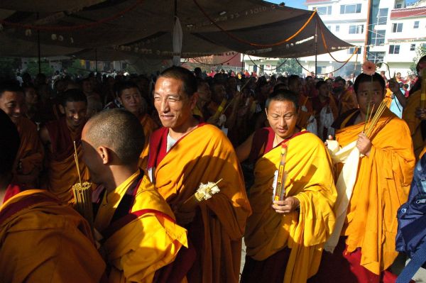 Senior lamas and tulku monks in their formal orange robes squint in the sun, holding incense and flowers for the procession around Tharlam Monastery of Tibetan Buddhism, Bodhisattva Day, Sakya Lamdre,...