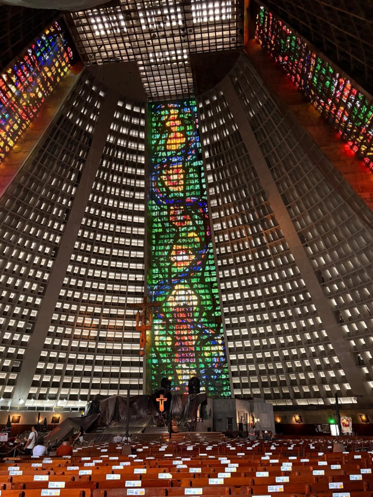 The image showcases the interior of a large, modern church or cathedral featuring impressive stained glass windows. The walls are lined with geometric shapes and large panes of colored glass that crea...