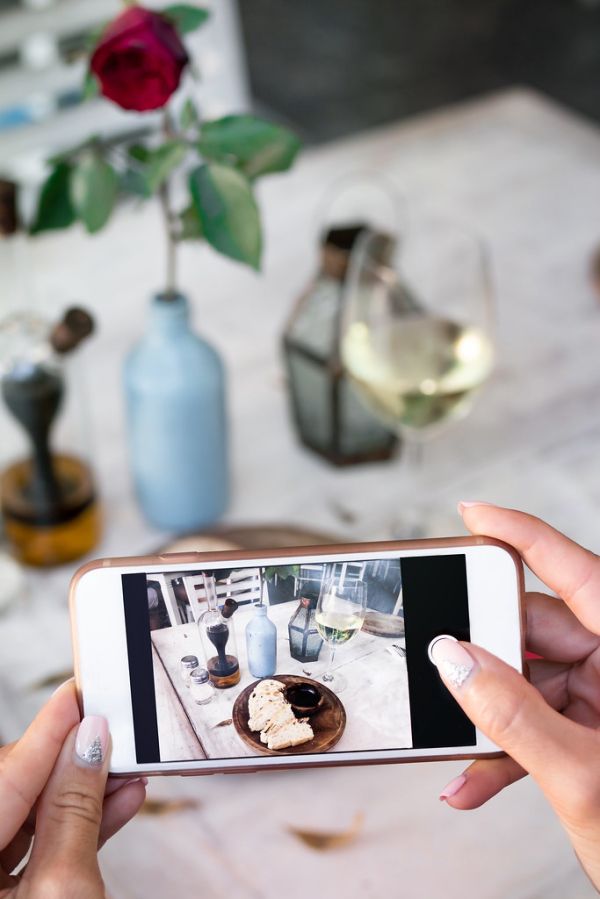 Woman taking photo of bread and wine on her smartphone in restaurant.