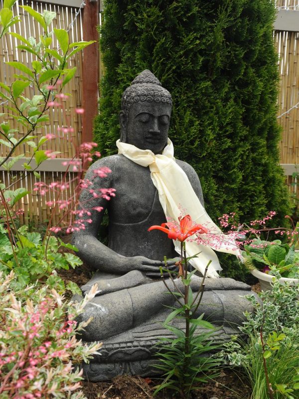Statue of Lord Buddha, meditation posture, Amitabha, wearing a blessed white Tibetan khata (kata), ritual scarf, Asiatic lily, plants, bamboo fence, Seattle, Washington, USA